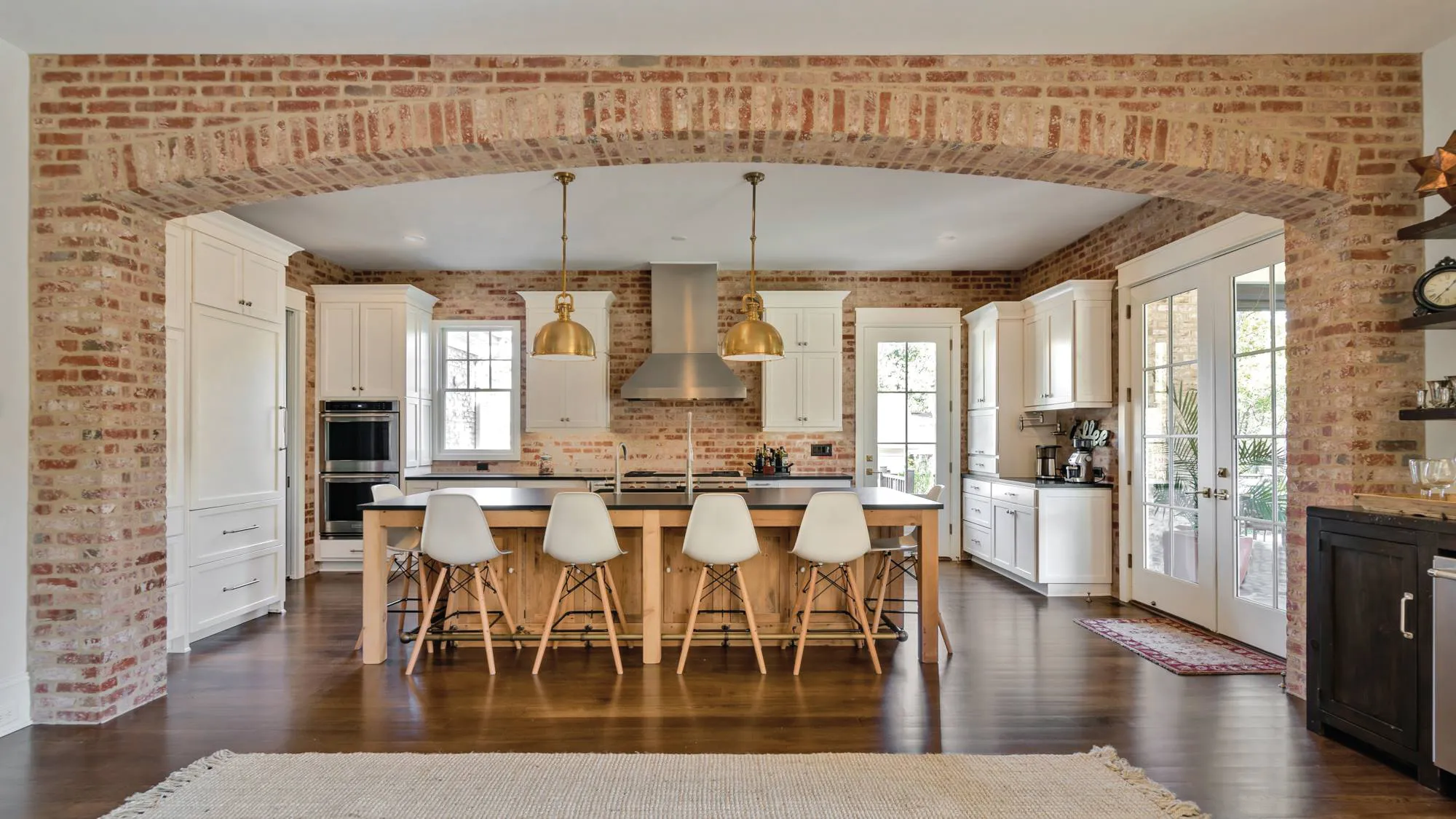 White cabinets and a wood-base island framed by a full brick archway
