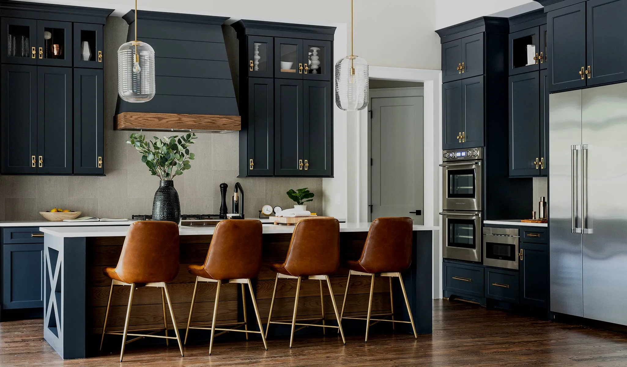 A midnight-blue Maple Shaker kitchen — shiplap hood with a wood band, brass pulls, leather stools