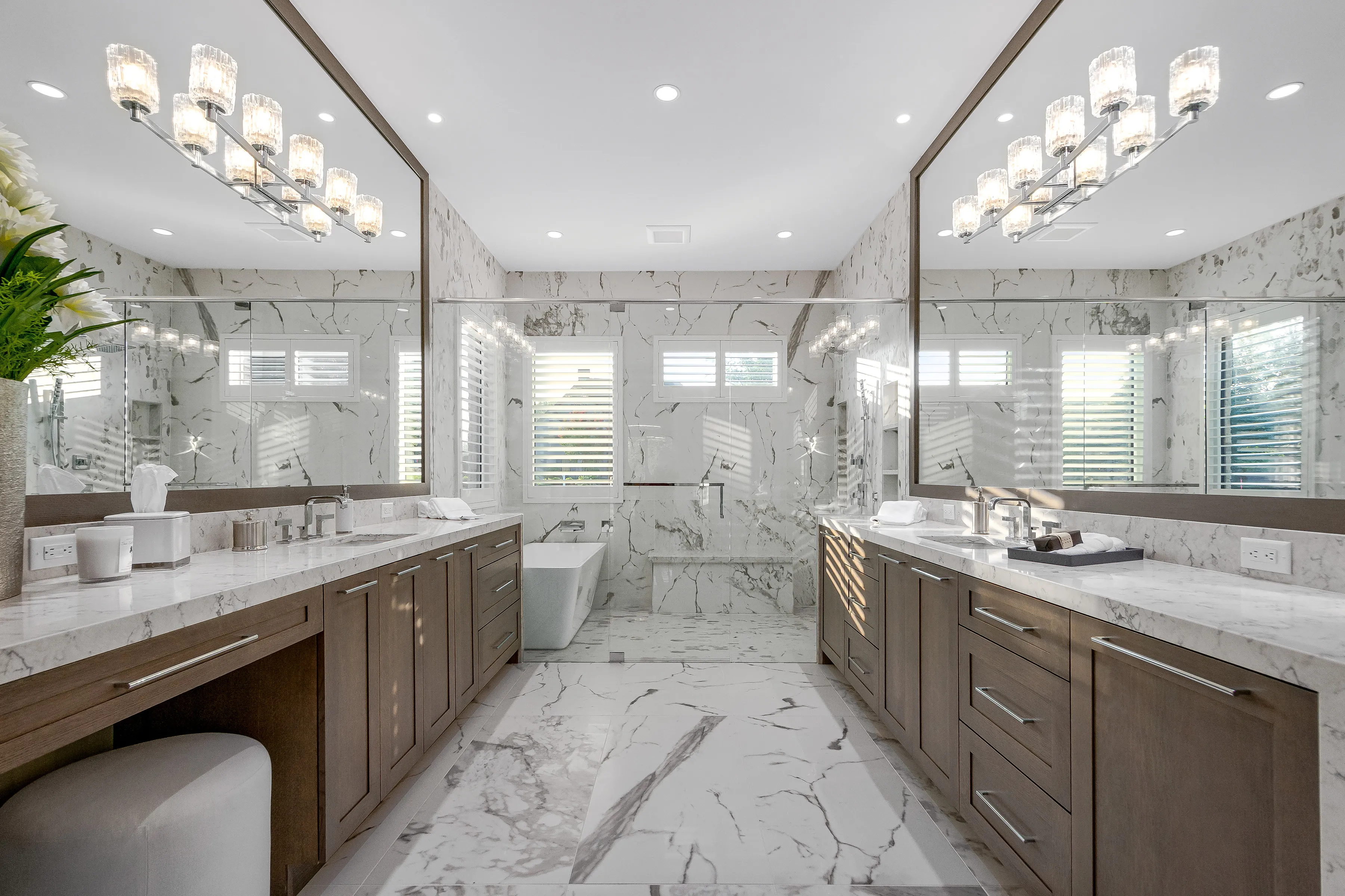 Marble master bath with dual wood vanities, a freestanding tub, and a glass shower