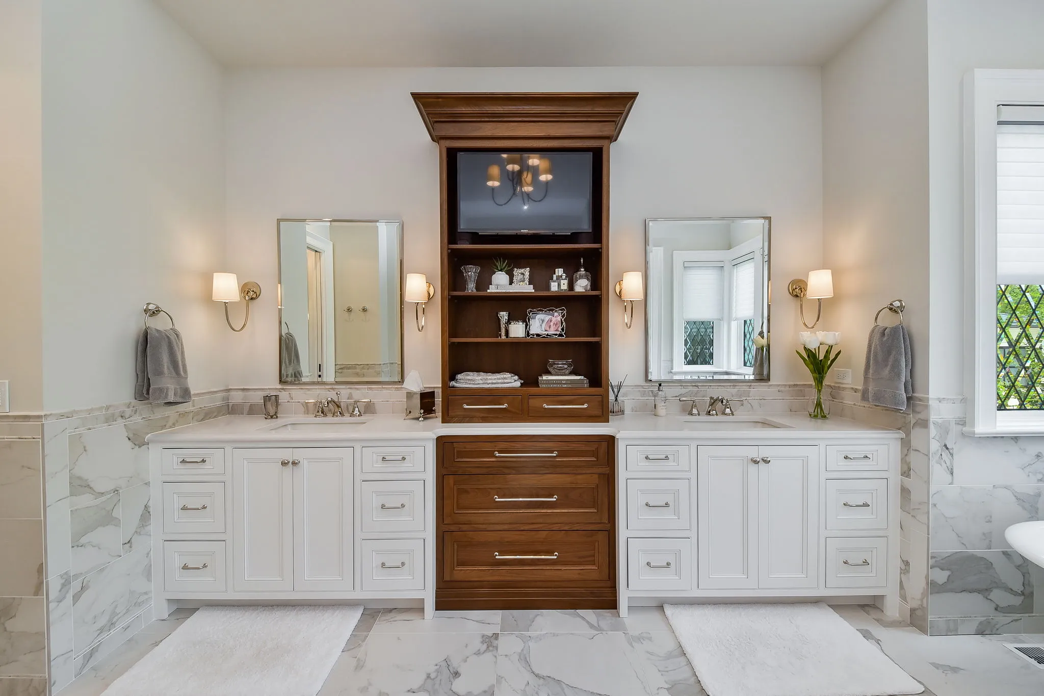 Twin white inset vanities flanking a walnut storage tower with open shelving