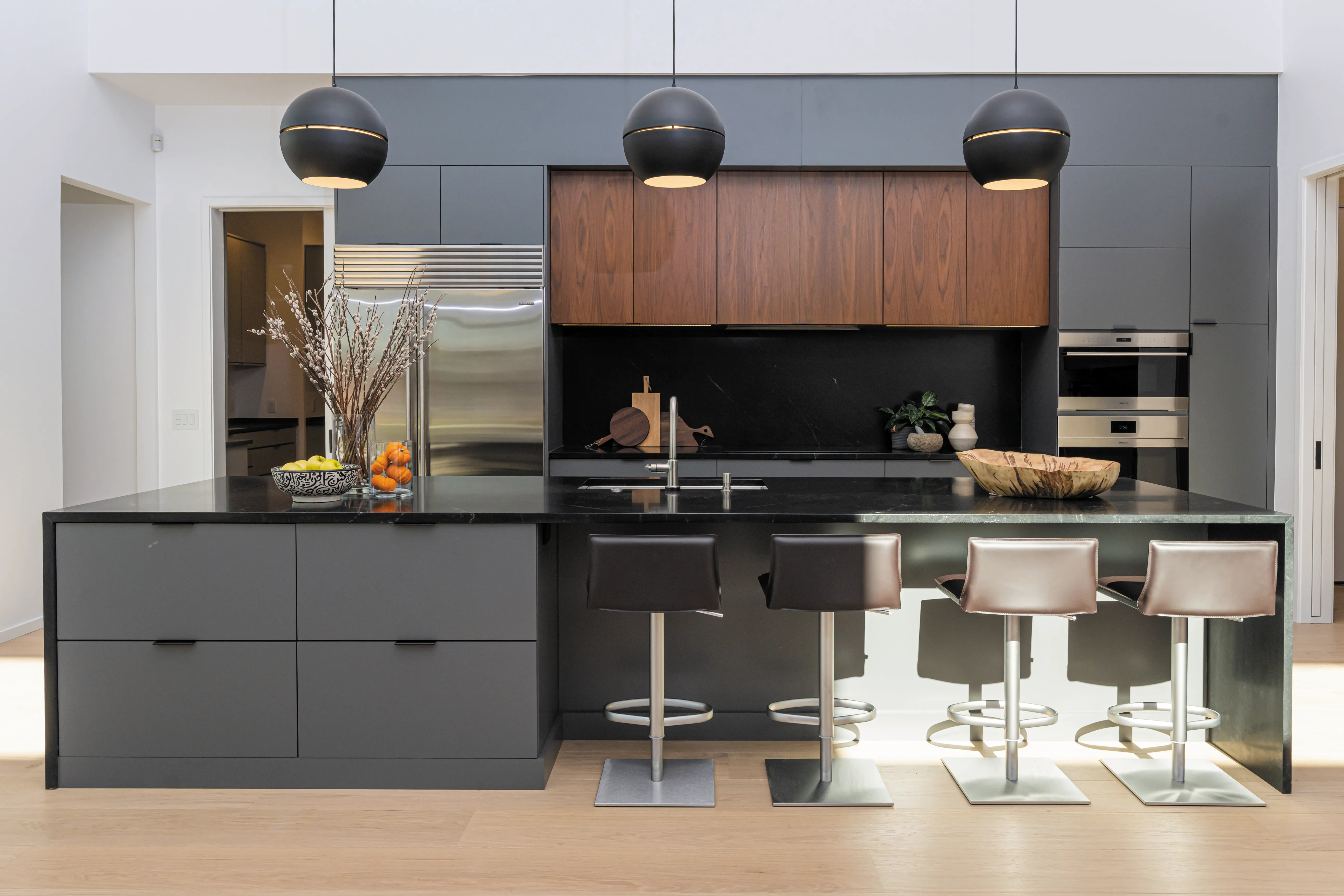 Graphite slab cabinets with walnut uppers and black globe pendants over a stone island