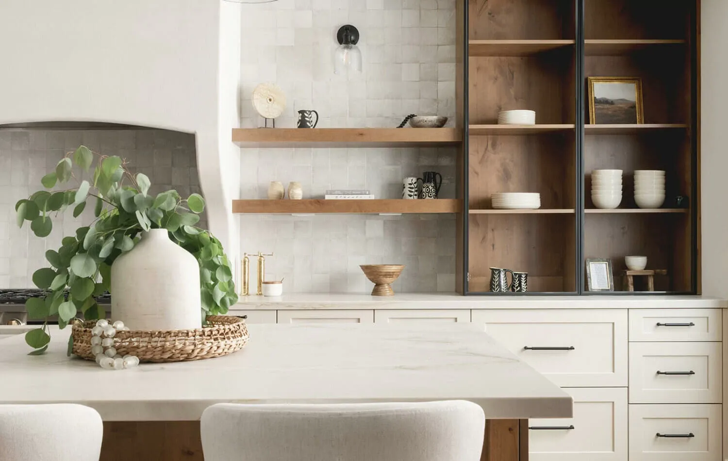 Warm white inset cabinets with a wood-and-black glass display cabinet, floating wood shelves, and a large island