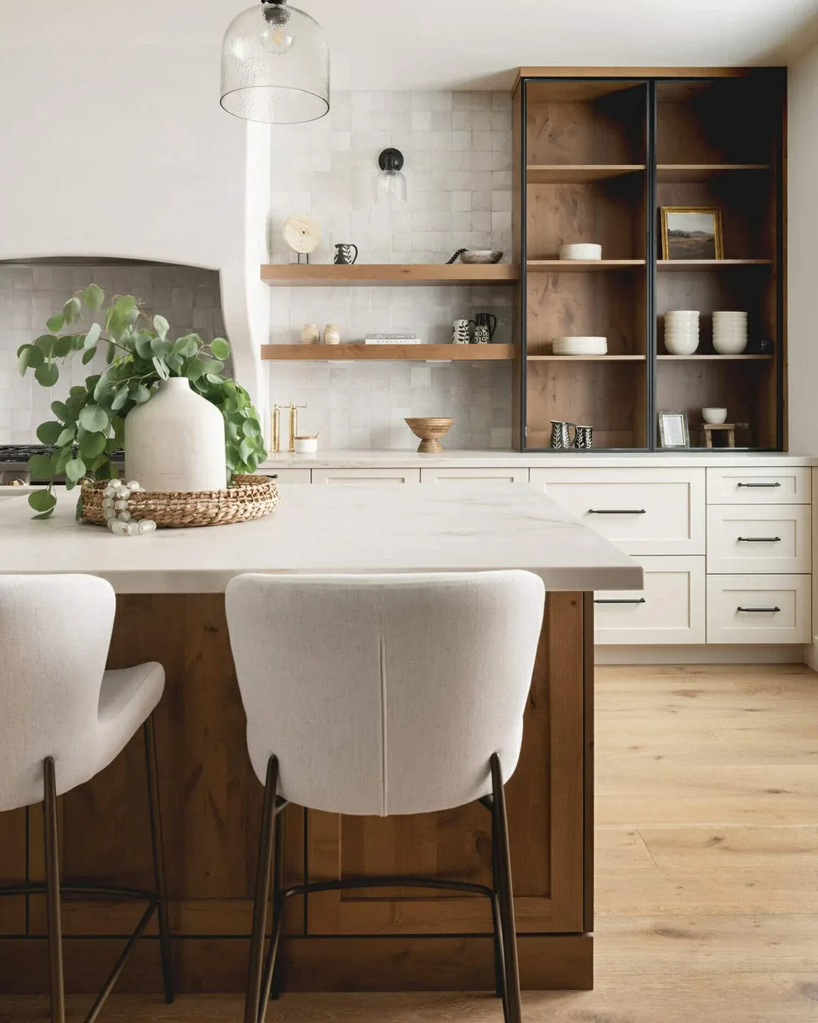 Prestige: warm white inset cabinets, a wood island with upholstered stools, floating shelves, and a tall wood-and-black glass display cabinet